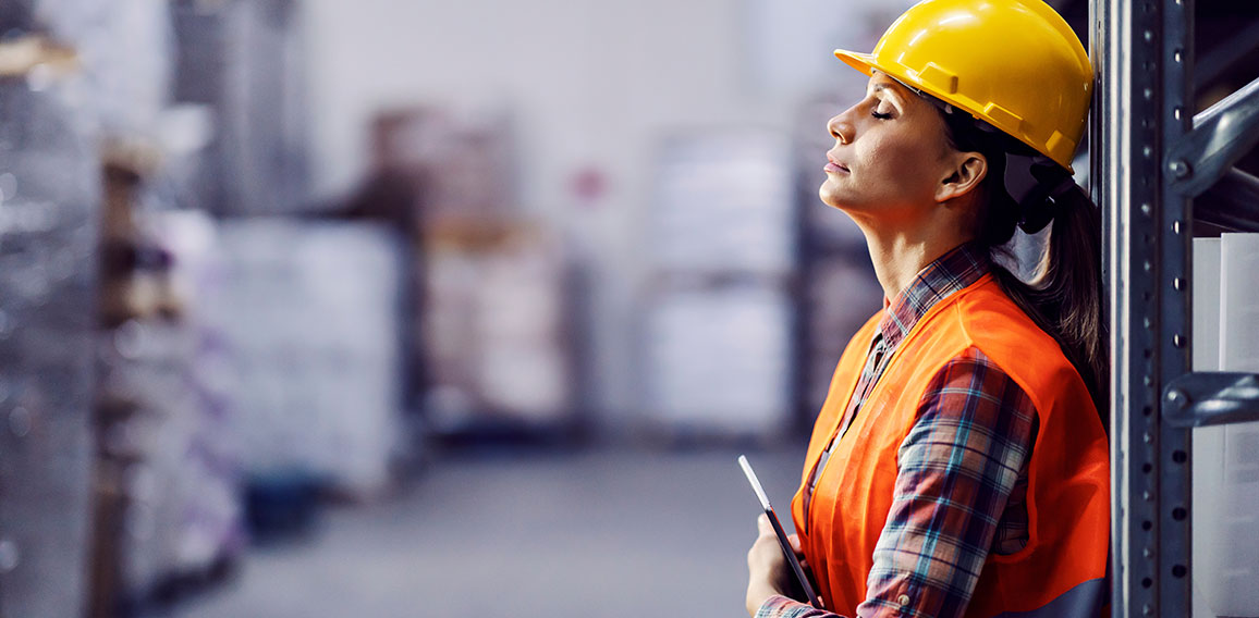 Tired female worker with tablet in hands leaning on shelf and ta