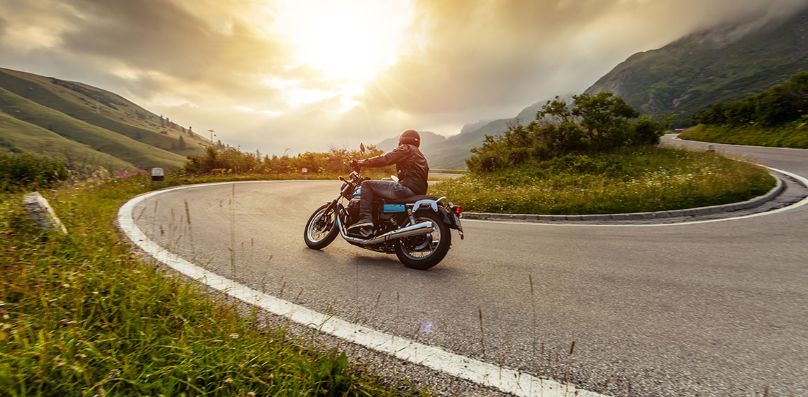 Motorcycle driver riding in Alpine landscape.