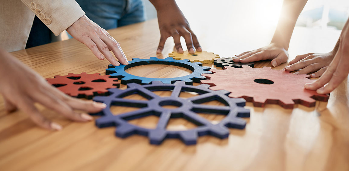 Hands, collaboration and gear with a business team working together in synergy for innovation at a workshop. Meeting, teamwork and creative with a man and woman employee group at work in the office