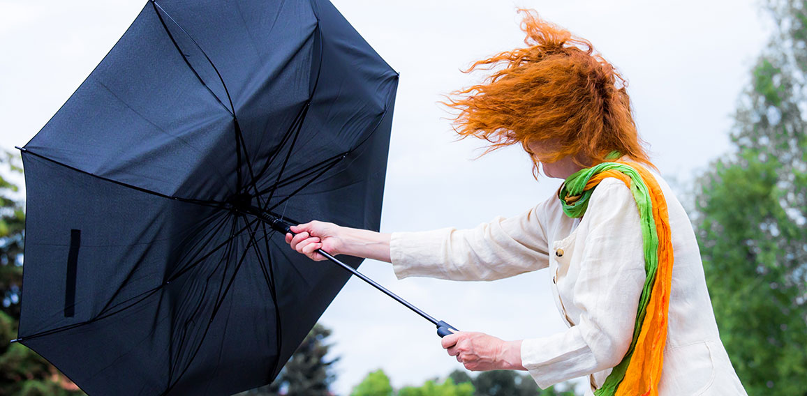 eine Frau mit roten Haaren versucht ihren Regenschirm festzuhalt