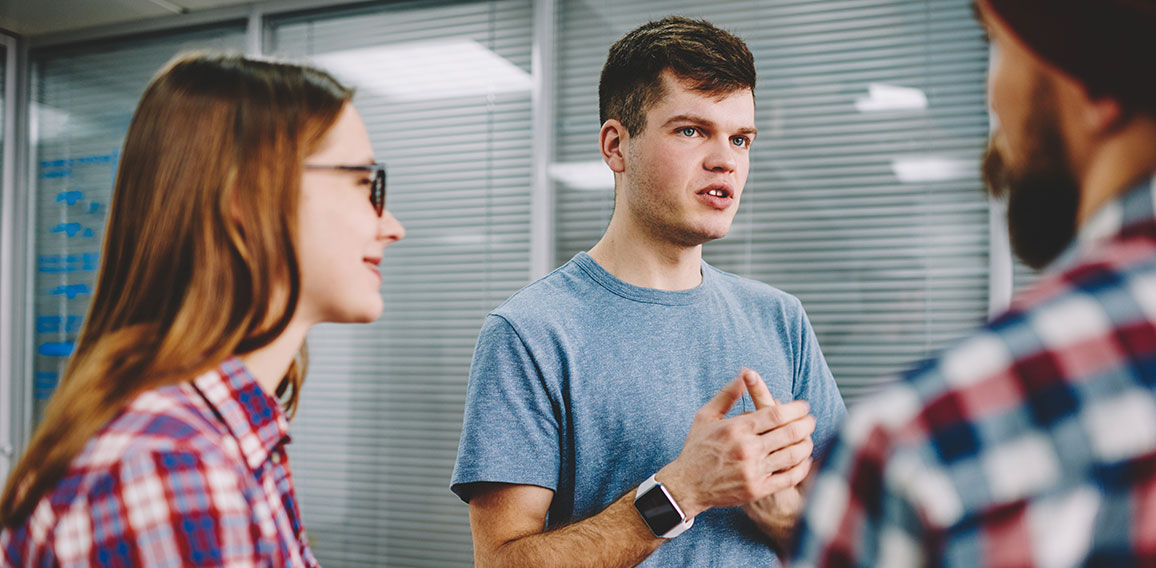 Serious hipster guy explaining study process to male and female