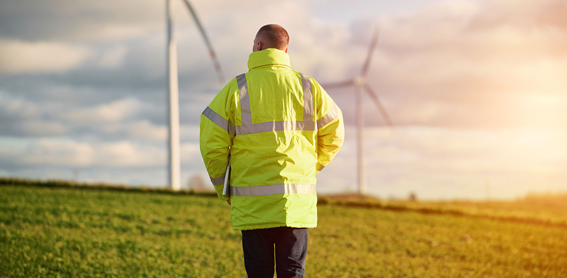 Back view of young male engineer in a wind turbine farm in the b