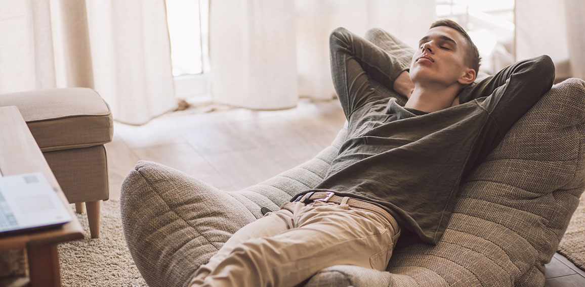 Handsome teenage guy relaxing on modern soft couch at home in li