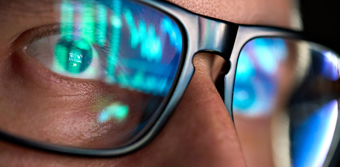 Trader looking at computer screen analyzing trading chart reflecting in glasses.