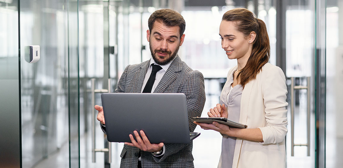 Businesswoman and businessman in laptop standing and discussing project in empty office windows with city view.