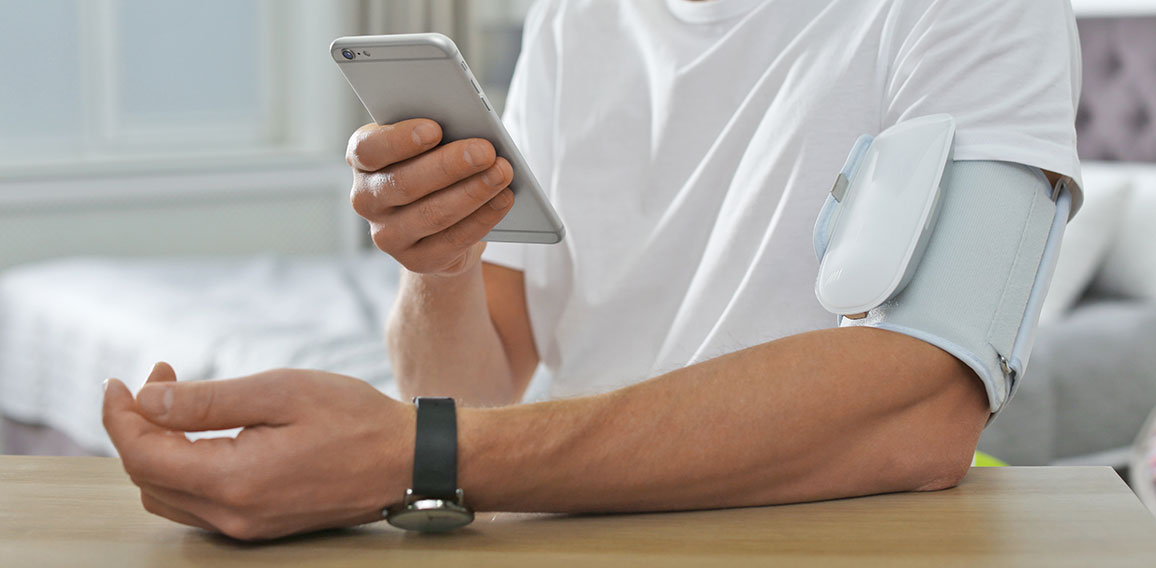 Man checking blood pressure with modern monitor and smartphone a