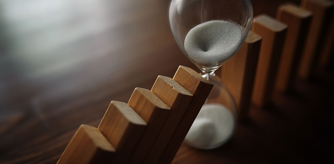 domino effect concept with wooden tiles blocked by hourglass wit