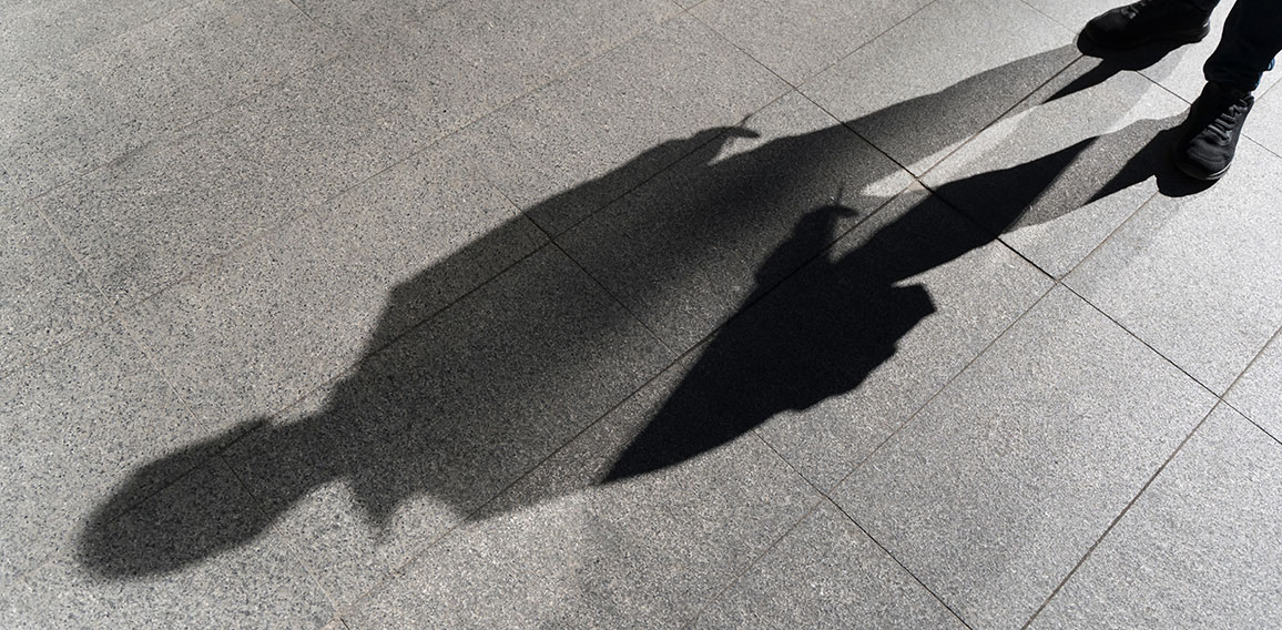 Dark shadow of a lonely person on the ground in the street. Stranger with a cigarette. Anxiety, depression, loneliness, fear concept.