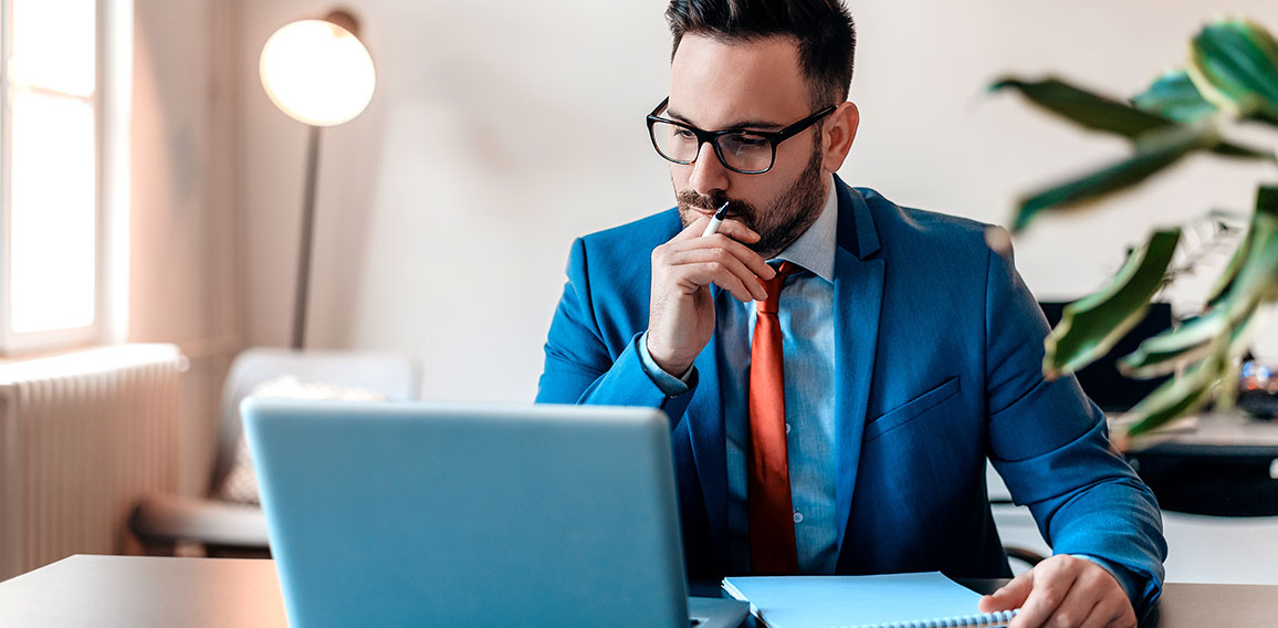 Young manager sitting at desk in bright office, working on lapto