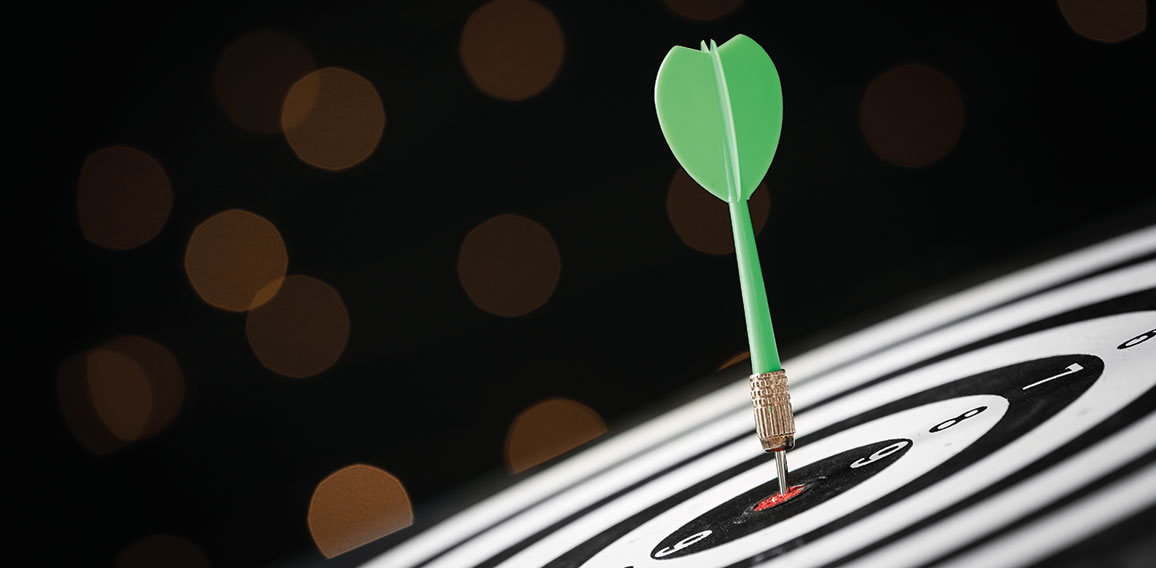 Green arrow hitting target on dart board against blurred lights.