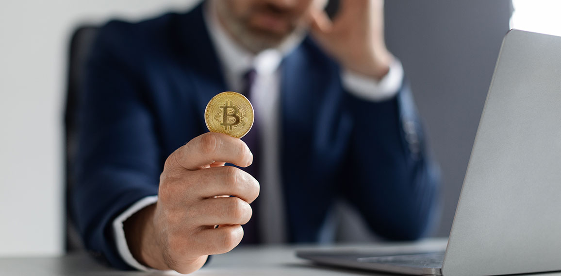 Crypto Failure. Upset Businessman Holding Bitcoin While Sitting At Desk With Laptop