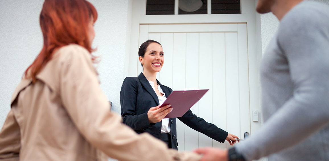 Real estate agent near door inviting young couple to enter house