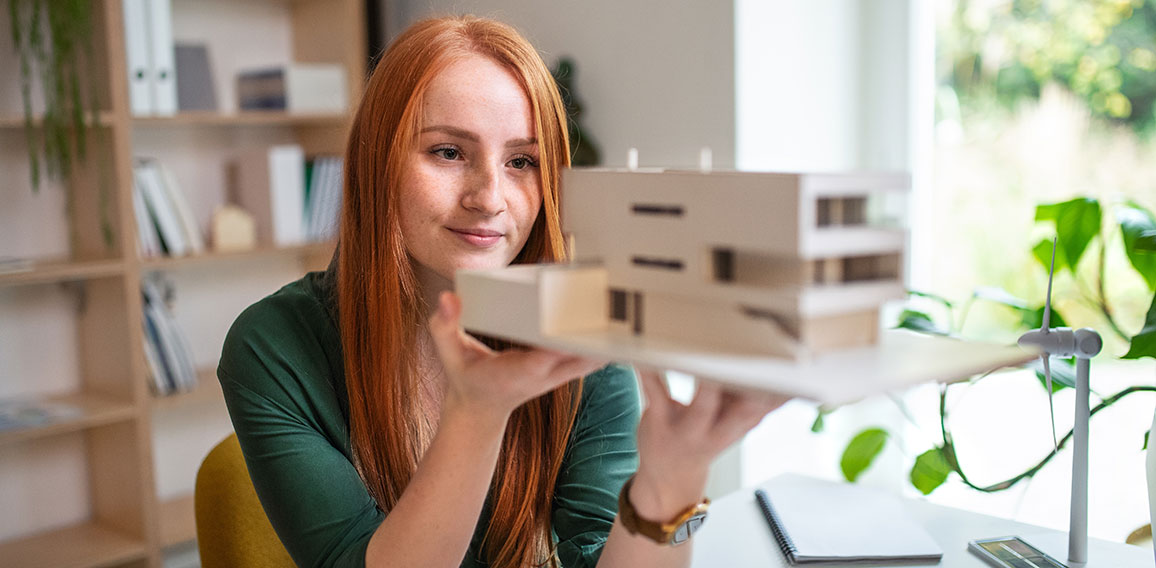 Architect with model of a house sitting at the desk indoors in office.