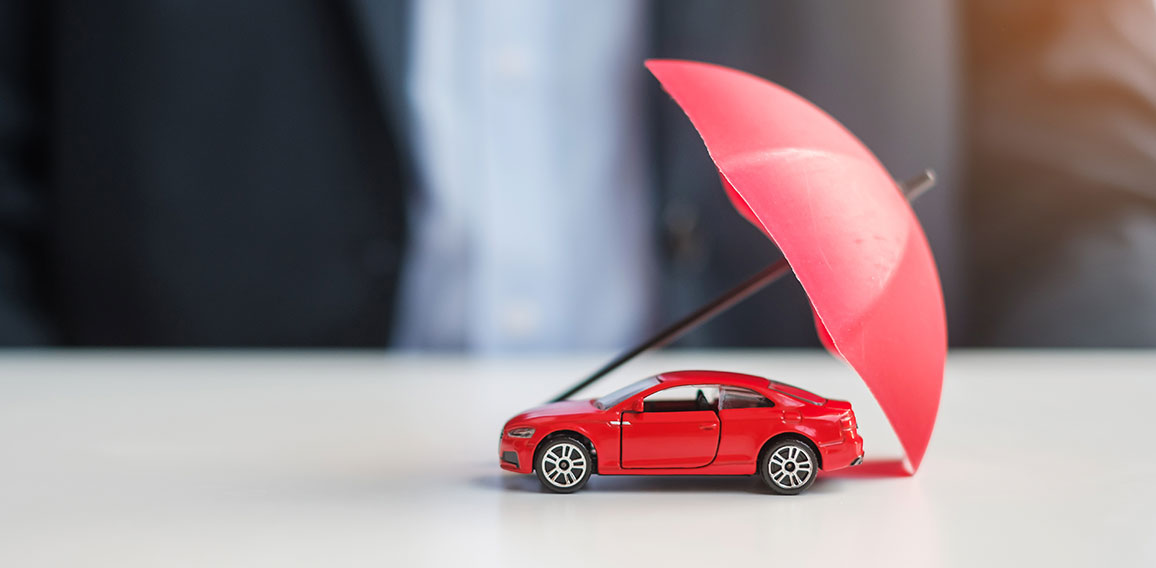 Businessman hand holding umbrella and cover  red car toy on tabl