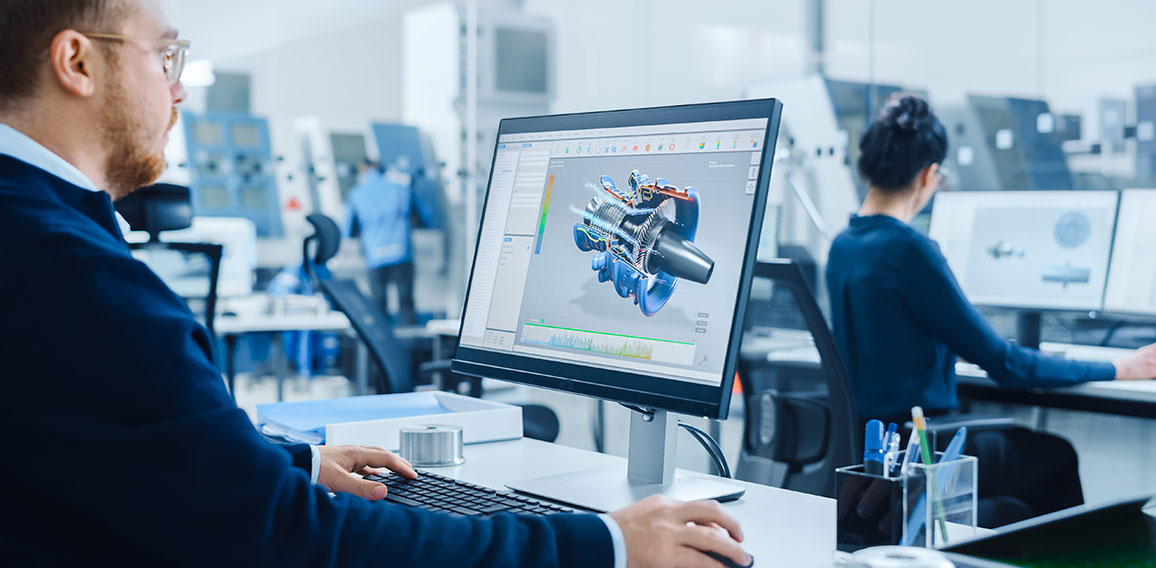 Over Shoulder: Heavy Industry Engineer Working on Personal Computer, Screen Shows CAD Software Showing New Generation Electric Engine. Industrial Factory with High-Tech CNC Machinery