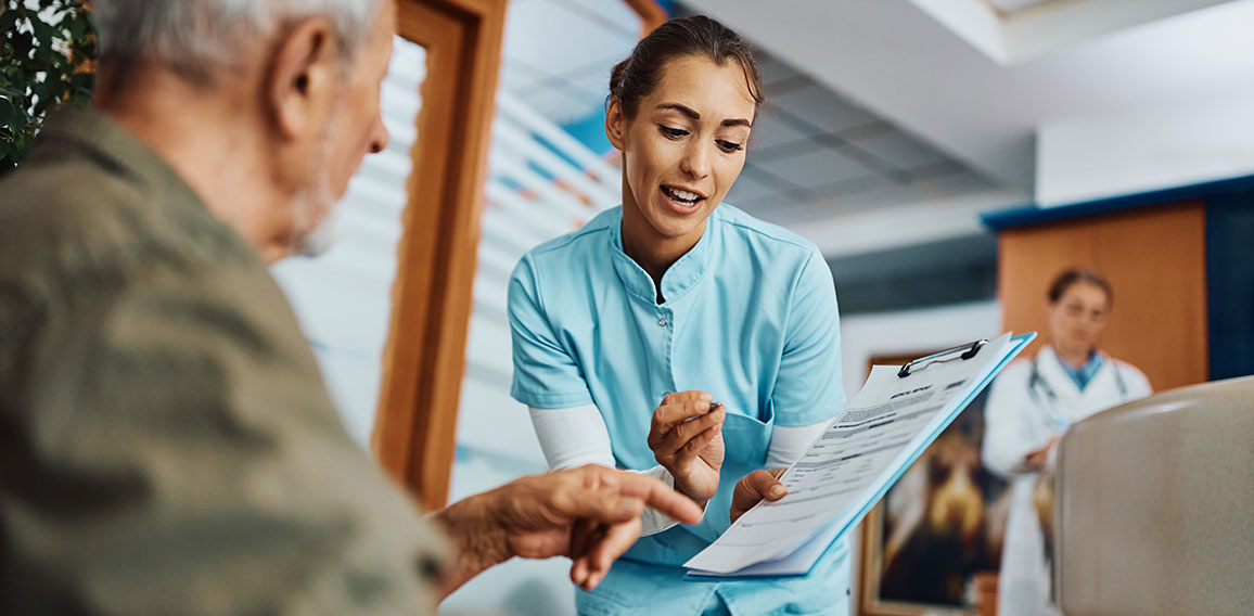 Young nurse assisting senior man in filling paperwork at doctor's office.