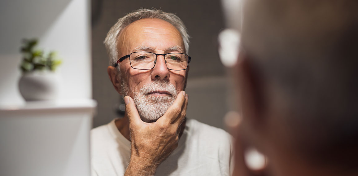 Senior man is looking at his face in bathroom and thinking about