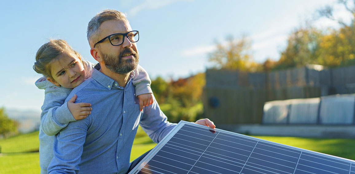 Father with his little daughter catching sun at solar panel,charging at their backyard. Alternative energy, saving resources and sustainable lifestyle concept.