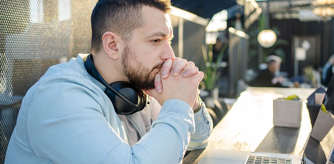 Portrait of unhappy male touching head with hands while looking at notebook computer in cafe