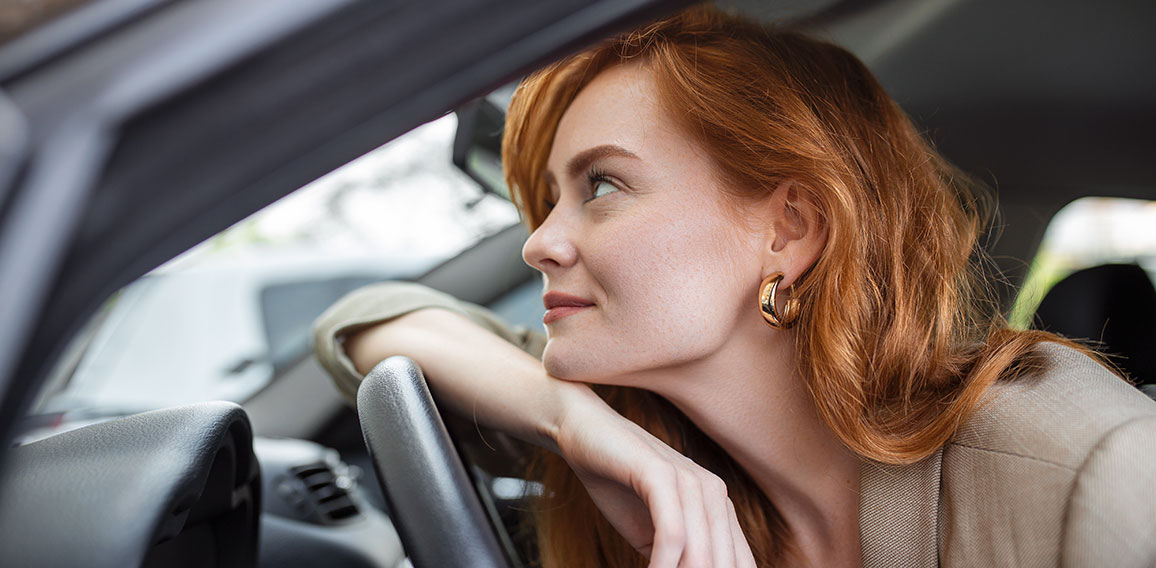 Young Woman Embracing Her New Car. Excited young woman and her new car indoors. Young and cheerful woman enjoying new car hugging steering wheel sitting inside