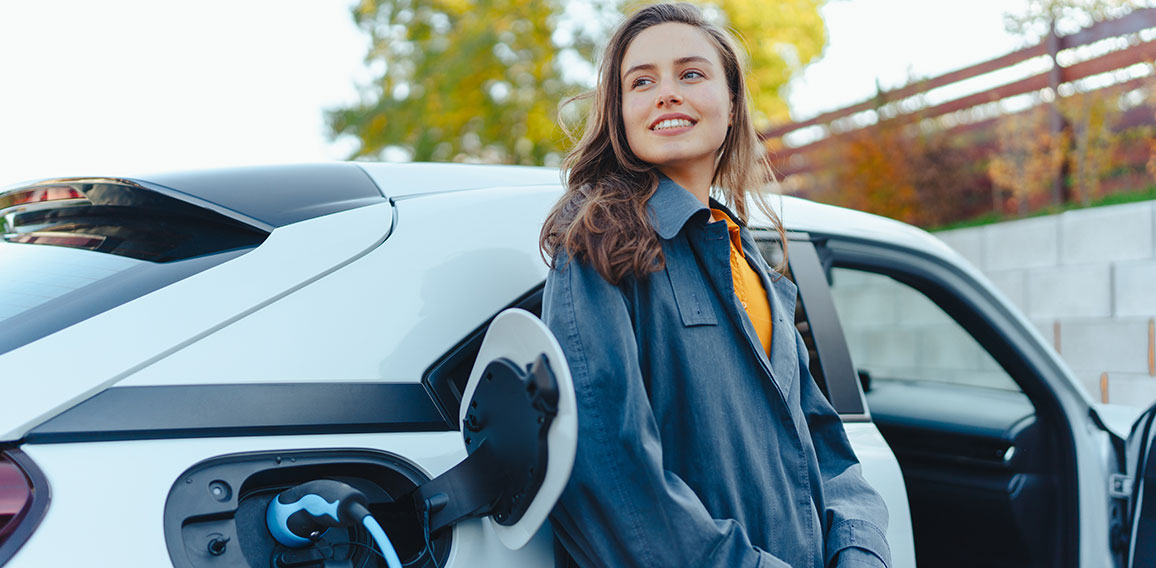 Young woman waiting while her electric car charging in home charging station, sustainable and economic transportation concept.