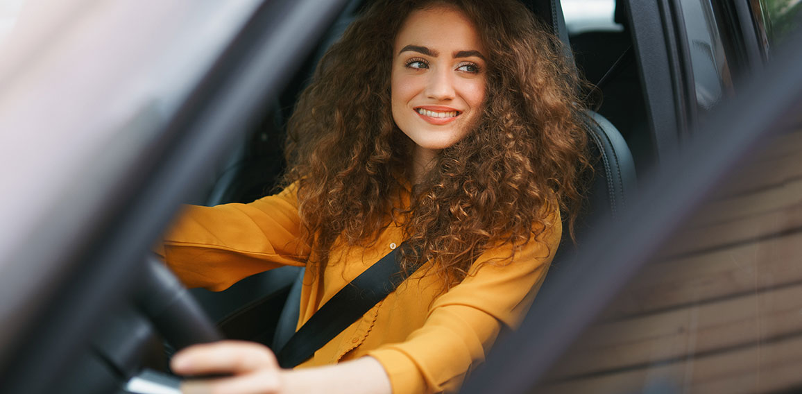 Young woman driving a car in the city. Portrait of a beautiful woman in a car, looking out of the window and smiling.