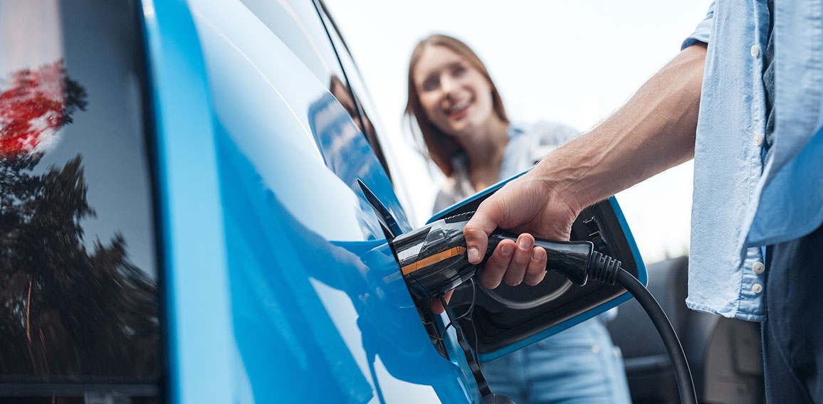 Young adult man charging blue electric car