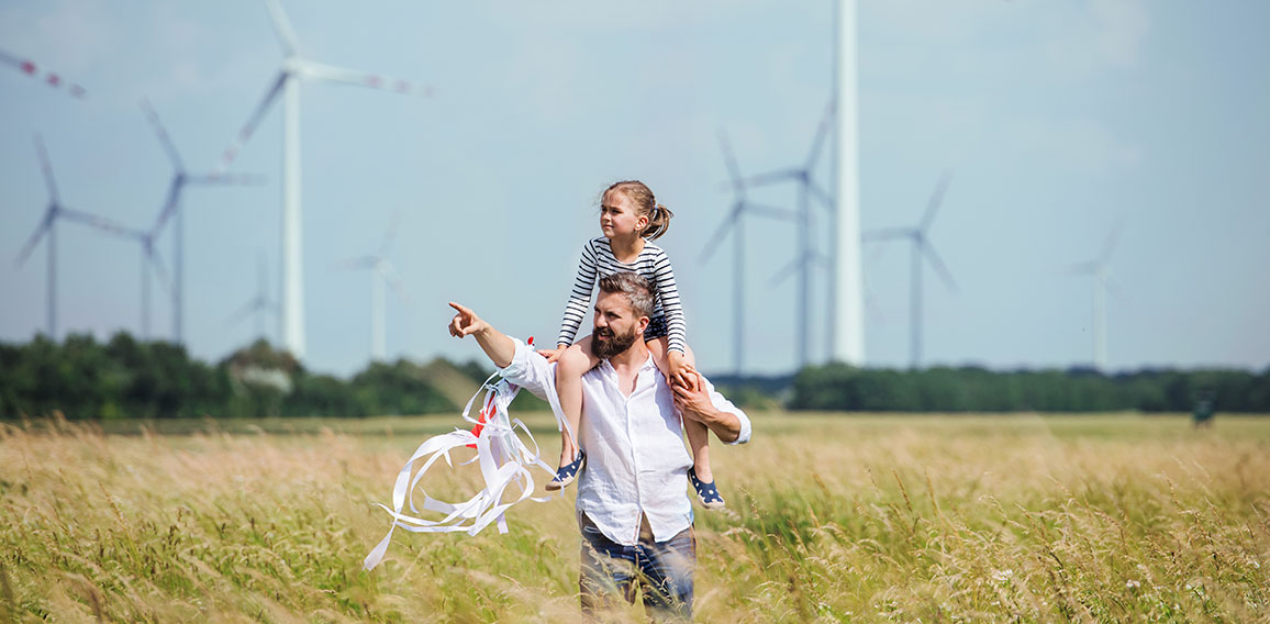 Mature father with small daughter walking on field on wind farm.