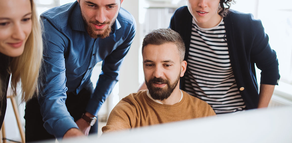 Group of young businesspeople looking at laptop screen in office, discussing issues.