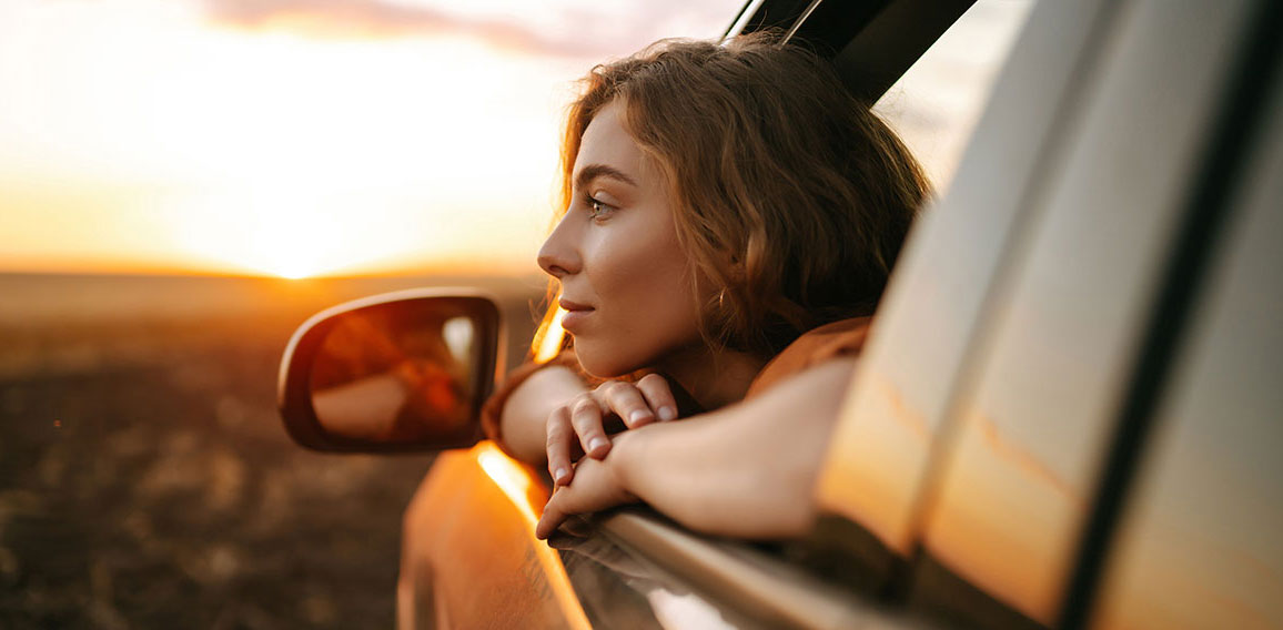 Happy woman outstretches her arms while sticking out the car win