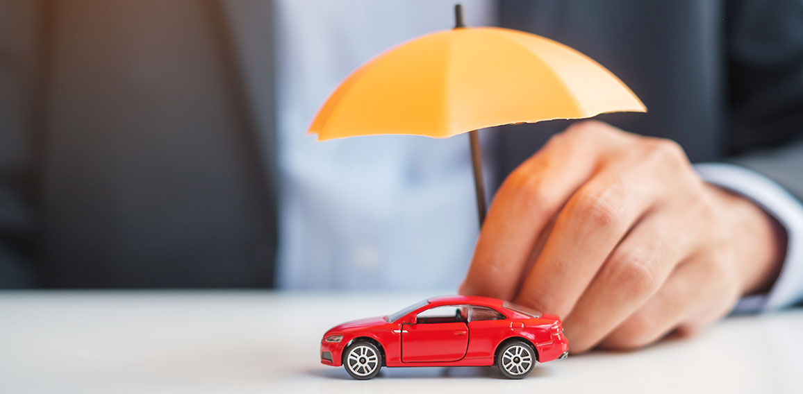 Businessman hand holding umbrella and cover  red car toy on tabl