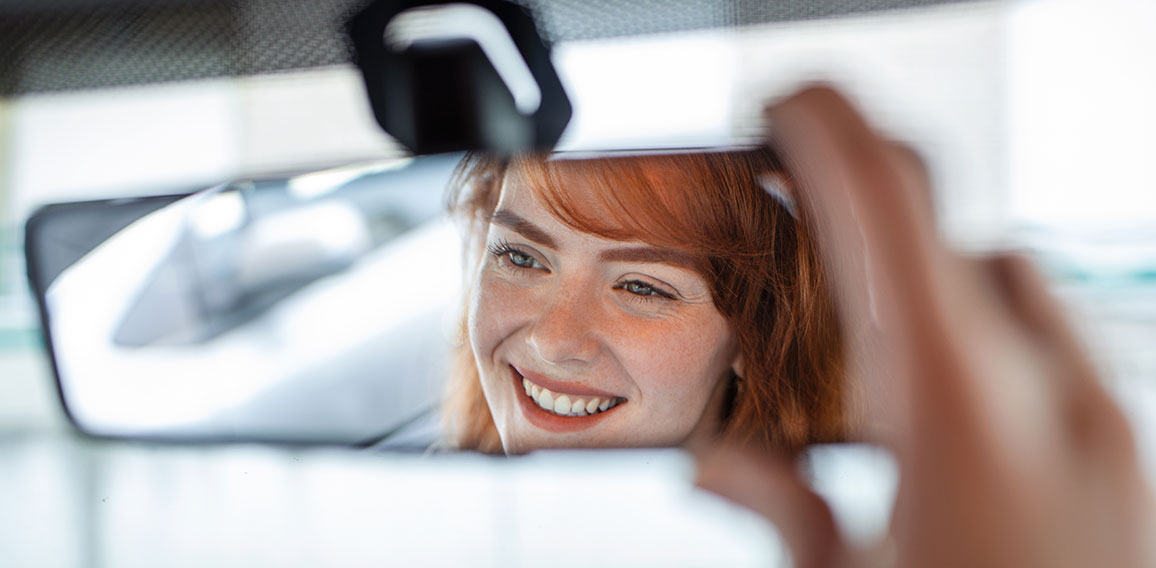 Woman hand adjusting rear view mirror of her car. Happy young woman driver looking adjusting rear view car mirror, making sure line is free visibility is good