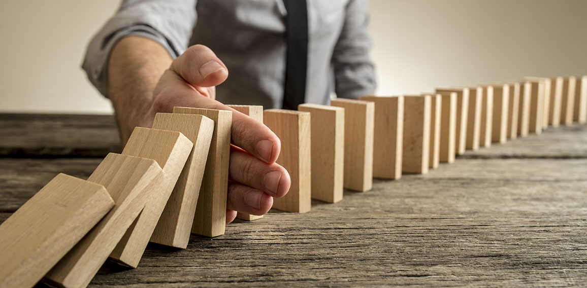 Man stopping domino effect on wooden table