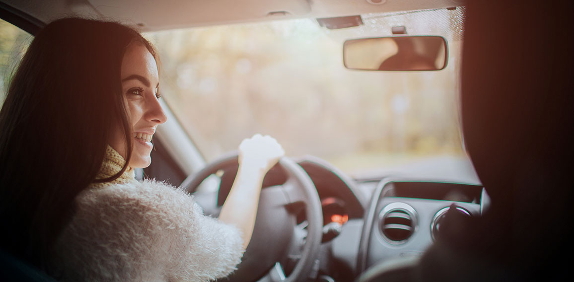 Long-haired brunette on the auto background. A female model is wearing a sweater and a scarf. Autumn concept. Autumn forest journey by car