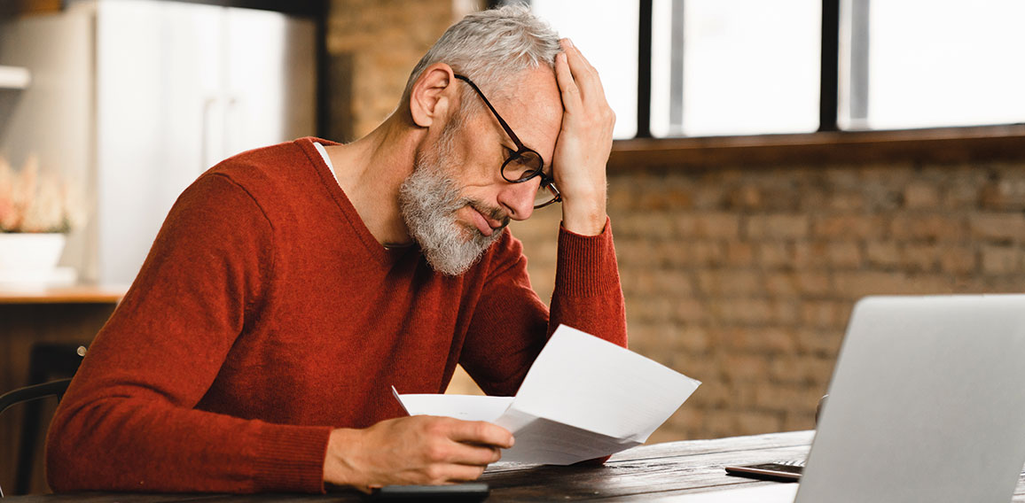 Expensive charges on domestic bills. Loan, debt, bunkruptcy concept. Sad depressed caucasian businessman holding documents, having problems with dismissal at home office