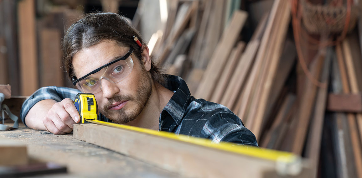 Male carpenter using measuring tape at the carpentry workshop. J