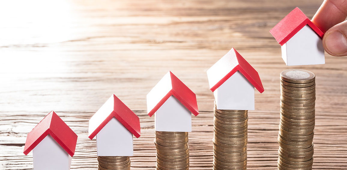 Person Placing House Models On Stacked Coins