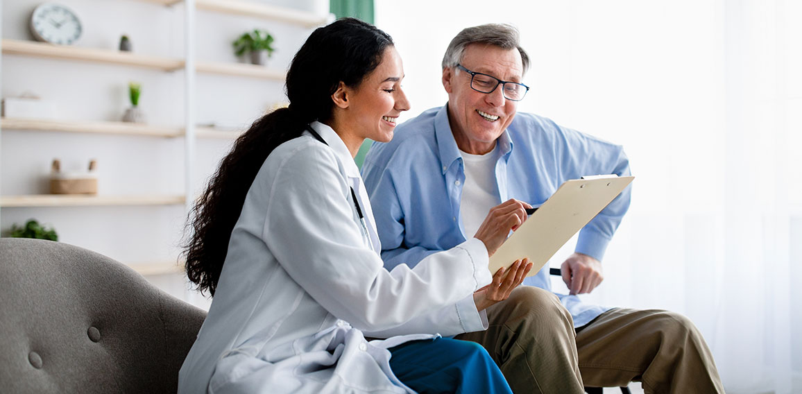 Young doctor asking senior impaired male patient in wheelchair to sign insurance policy at home