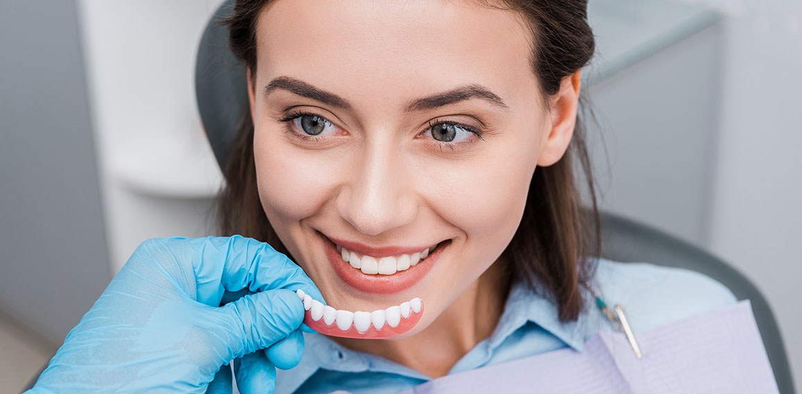 cropped view of dentist holding prosthesis near happy girl in dental clinic