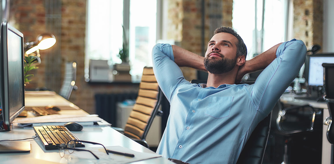 Enjoying break. Satisfied young bearded businessman leaning back with hands behind head and relaxing while sitting in the modern office