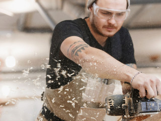 Carpenter working with electric planer on wooden plank in workshop. Hands and planer close up.