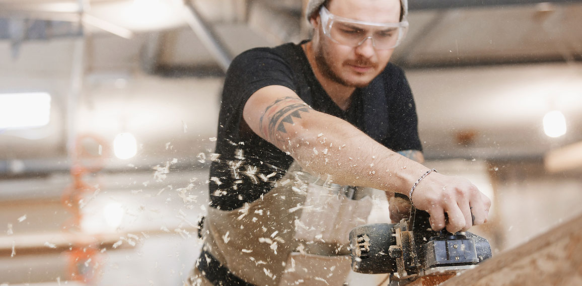 Carpenter working with electric planer on wooden plank in workshop. Hands and planer close up.