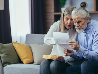 Angry frustrated document senior couple. Unhappy old family getting stressed. Serious older husband showing banking paper document bills taxes to confused elderly wife in home. Worried looking utility