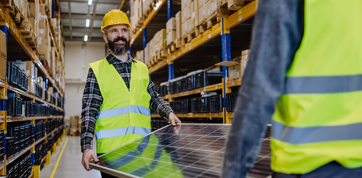 Warehouse workers in reflective vests carring a solar panel.