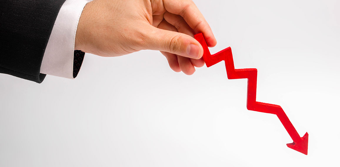 A businessman's hand is holding a red arrow down on a white background. The concept of reducing costs and profits, falling living standards and prices. Decreased projections, depressed economies.