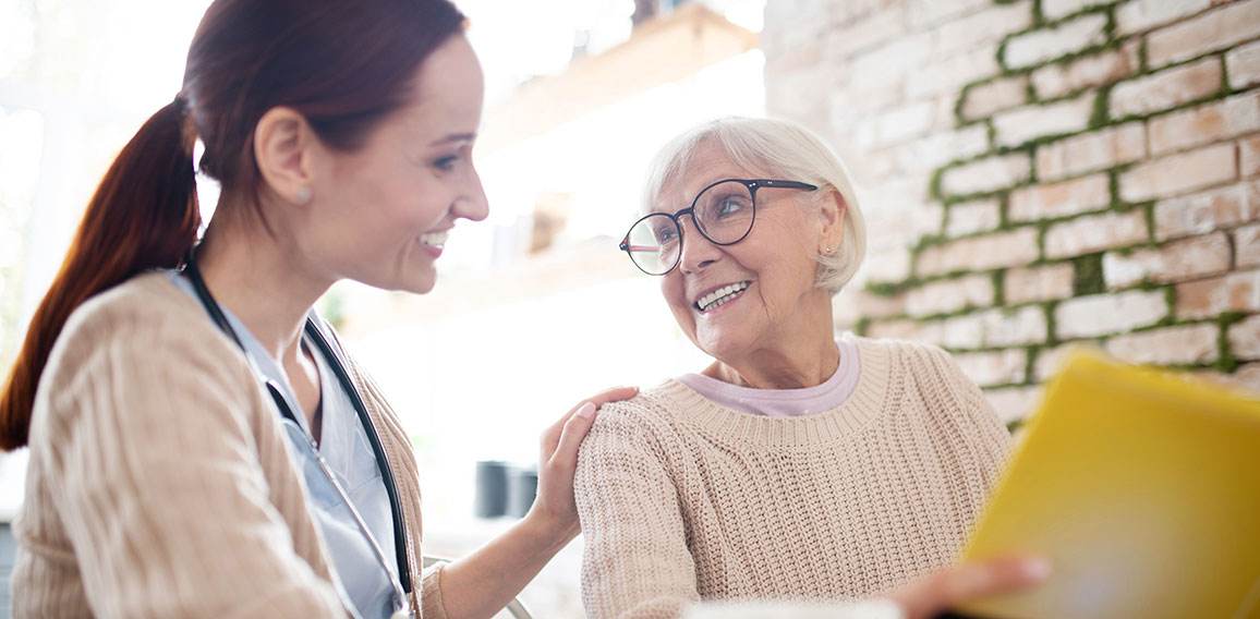 Red-haired nurse smiling while talking to kind aged woman