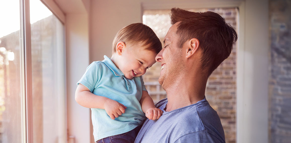 Father holds toddler son while drinking coffee at home, by the w