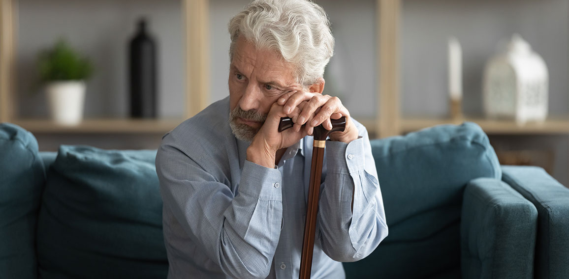 Tired upset mature man holding walking stick, sitting on couch