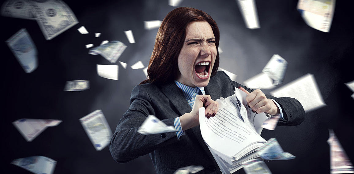 Young stressed woman ripping documents with frustrated facial expression.