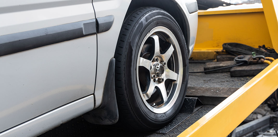 Broken down car towed onto flatbed tow truck with hook cable